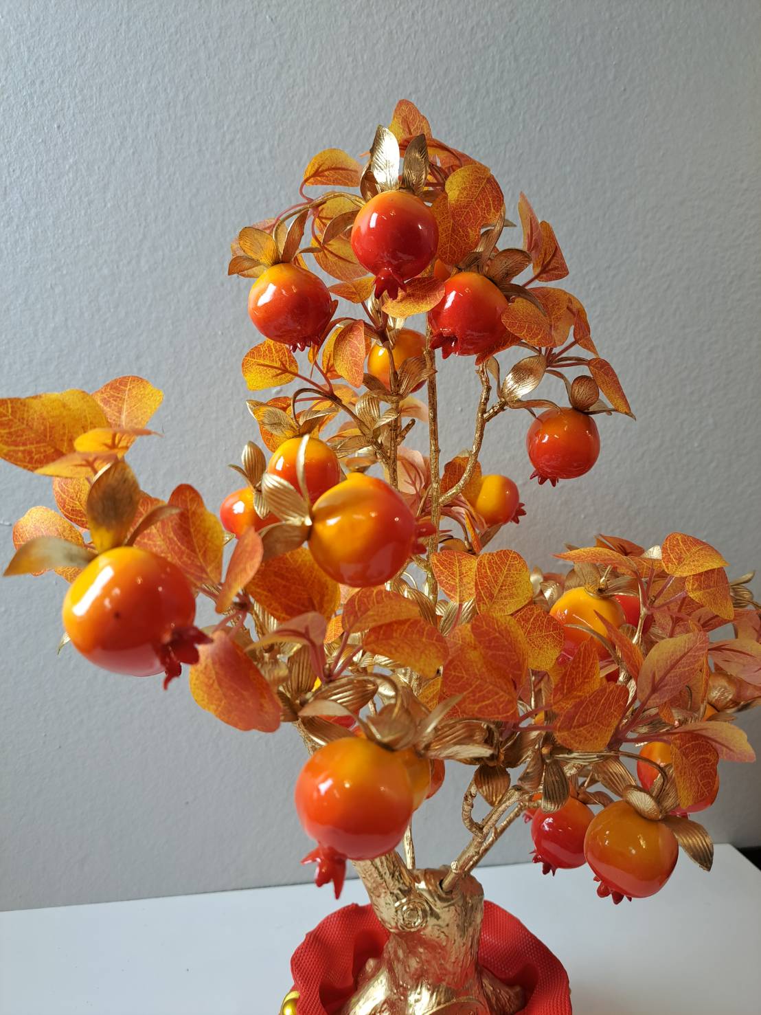 Close-up of glossy faux red and orange pomegranate fruits with amber autumn leaves on Artificial Fruit Tree N25