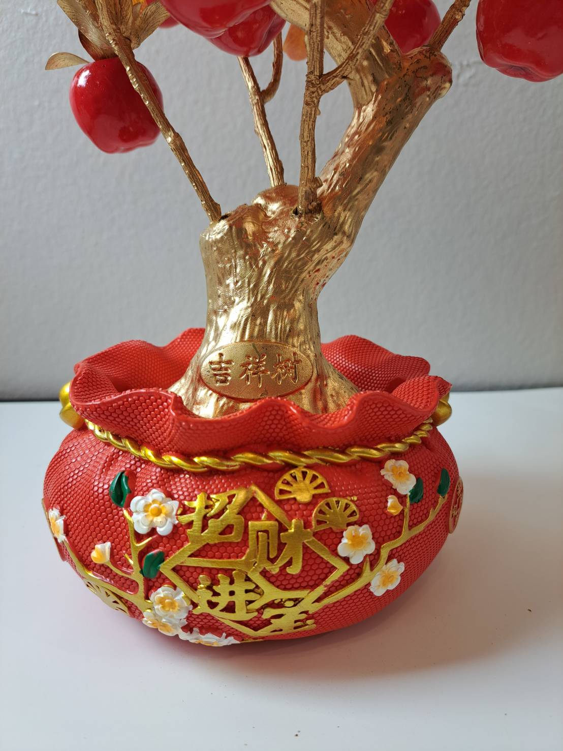 Close-up of decorative red ornamental pot with gold raised 招财进宝 characters, plum blossom accents and rope trim on Artificial Apple Tree N27