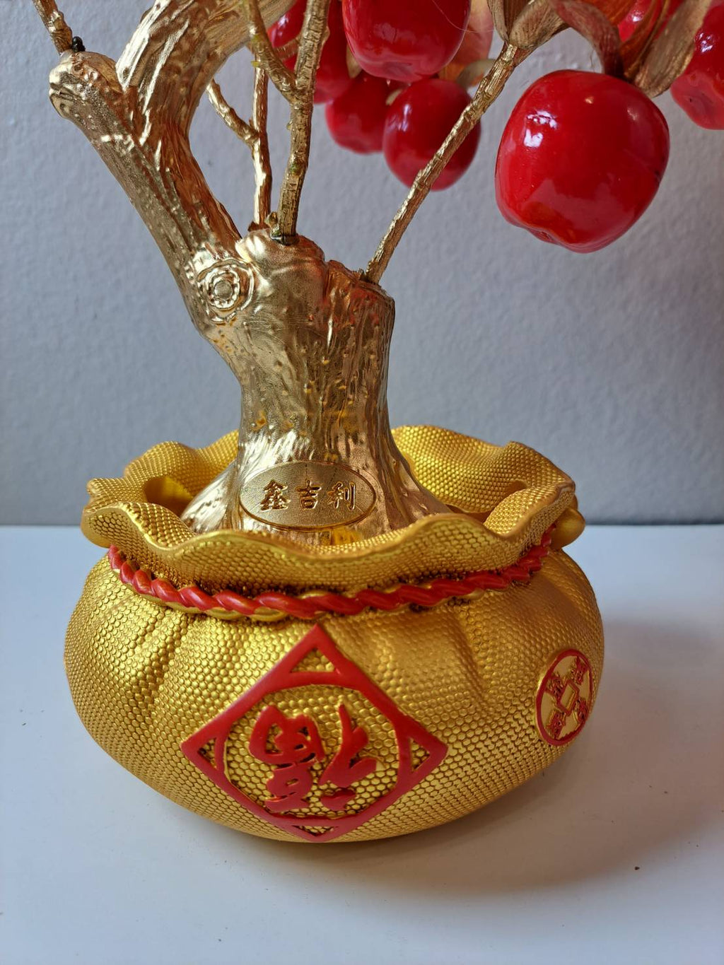 Close-up of decorative golden ornamental pot with red raised 大吉大利 characters, plum blossom accents and rope trim on Artificial Apple Tree N28