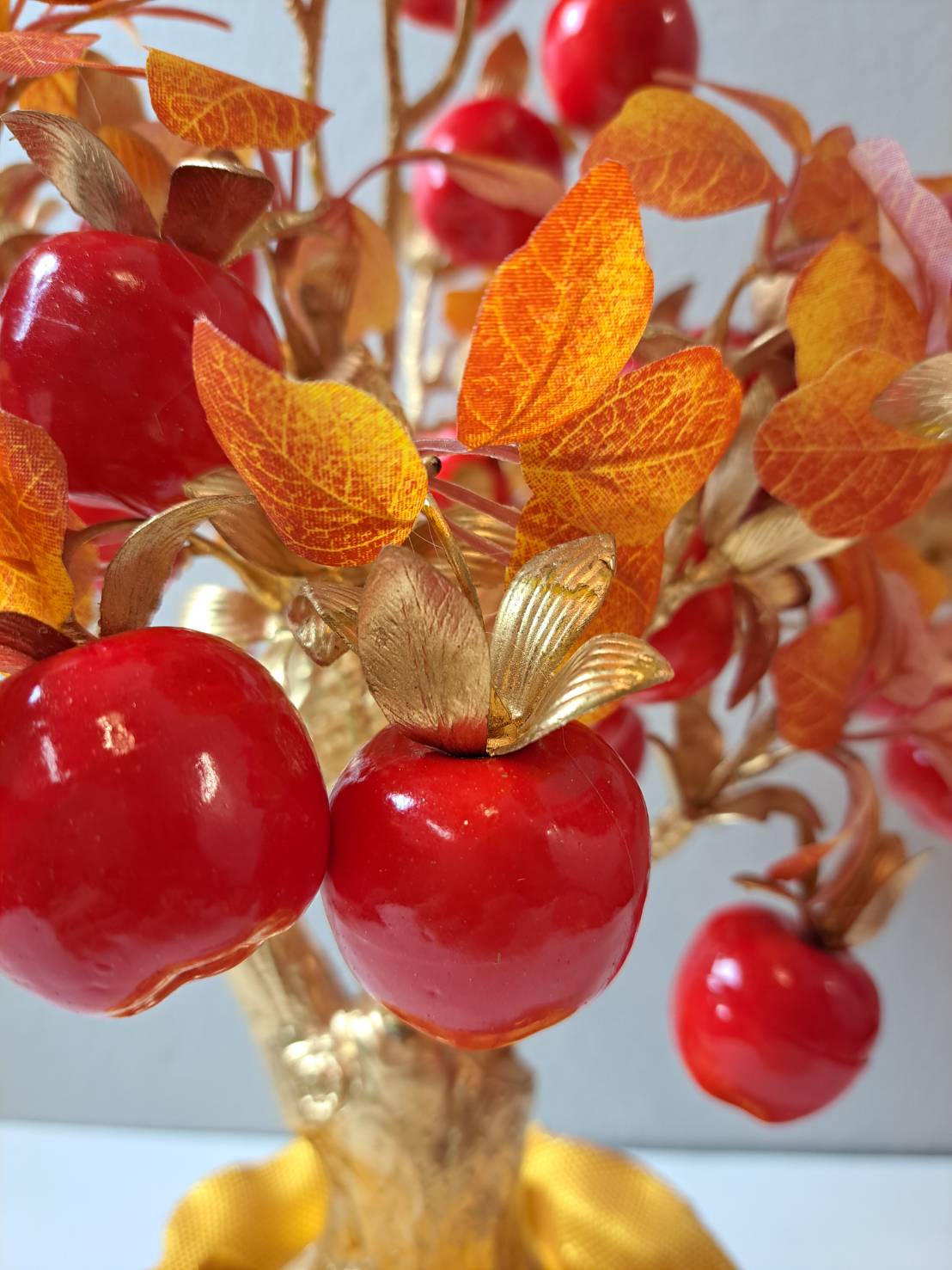Close-up of glossy faux red apples with amber and orange autumn leaves and gold petal accents on Artificial Apple Tree N28