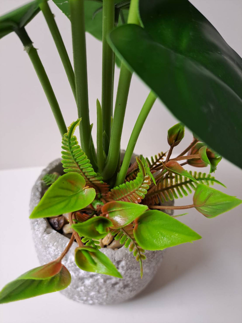 Faux anthurium base close-up with ferns and pebbles in terrazzo pot