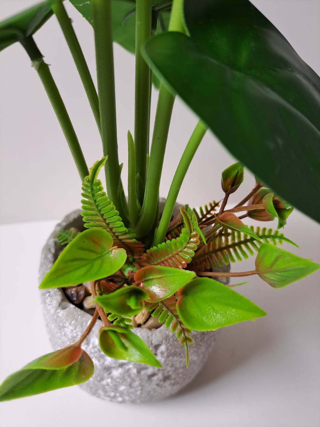 Faux anthurium base close-up with ferns and pebbles in terrazzo pot
