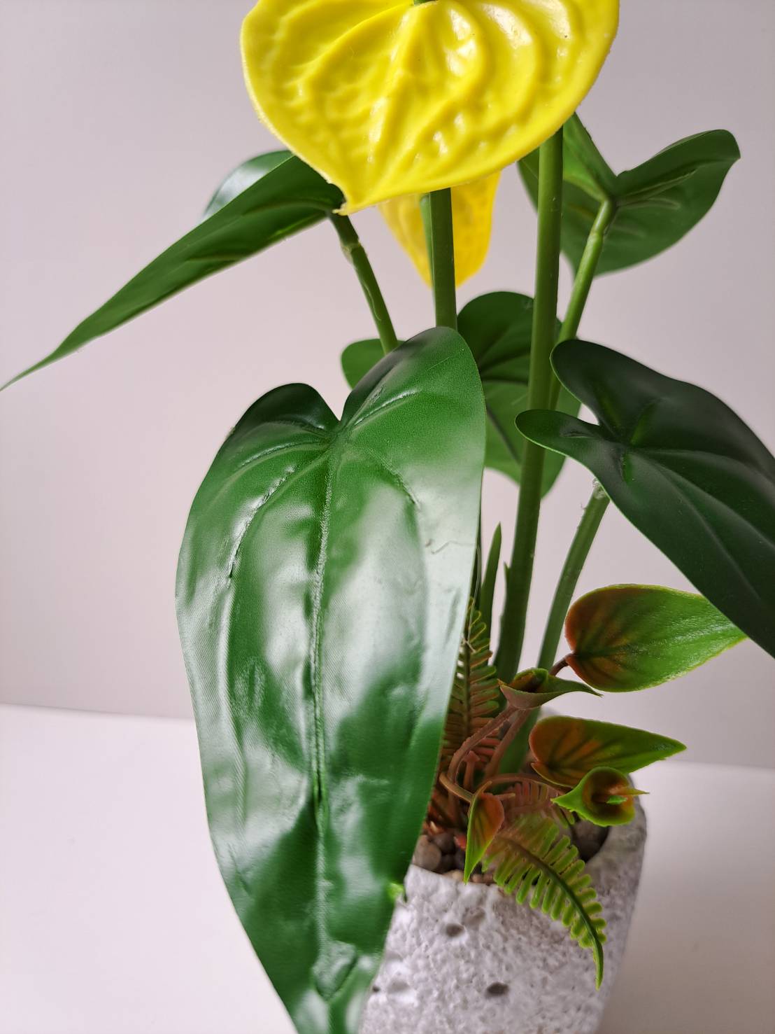 Faux yellow anthurium base close-up with ferns and pebbles in terrazzo pot