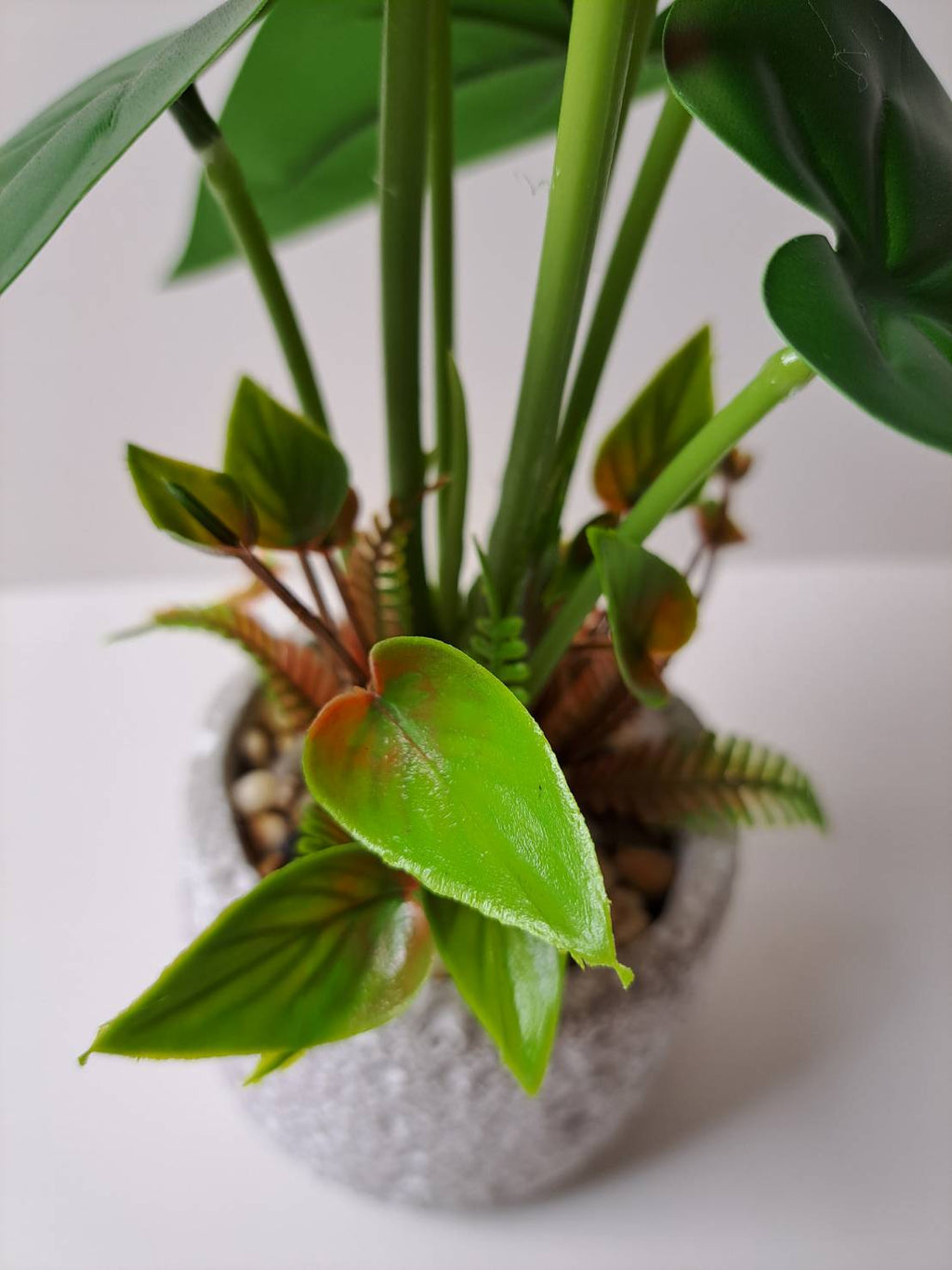 Faux anthurium base close-up with ferns and pebbles in terrazzo stone pot