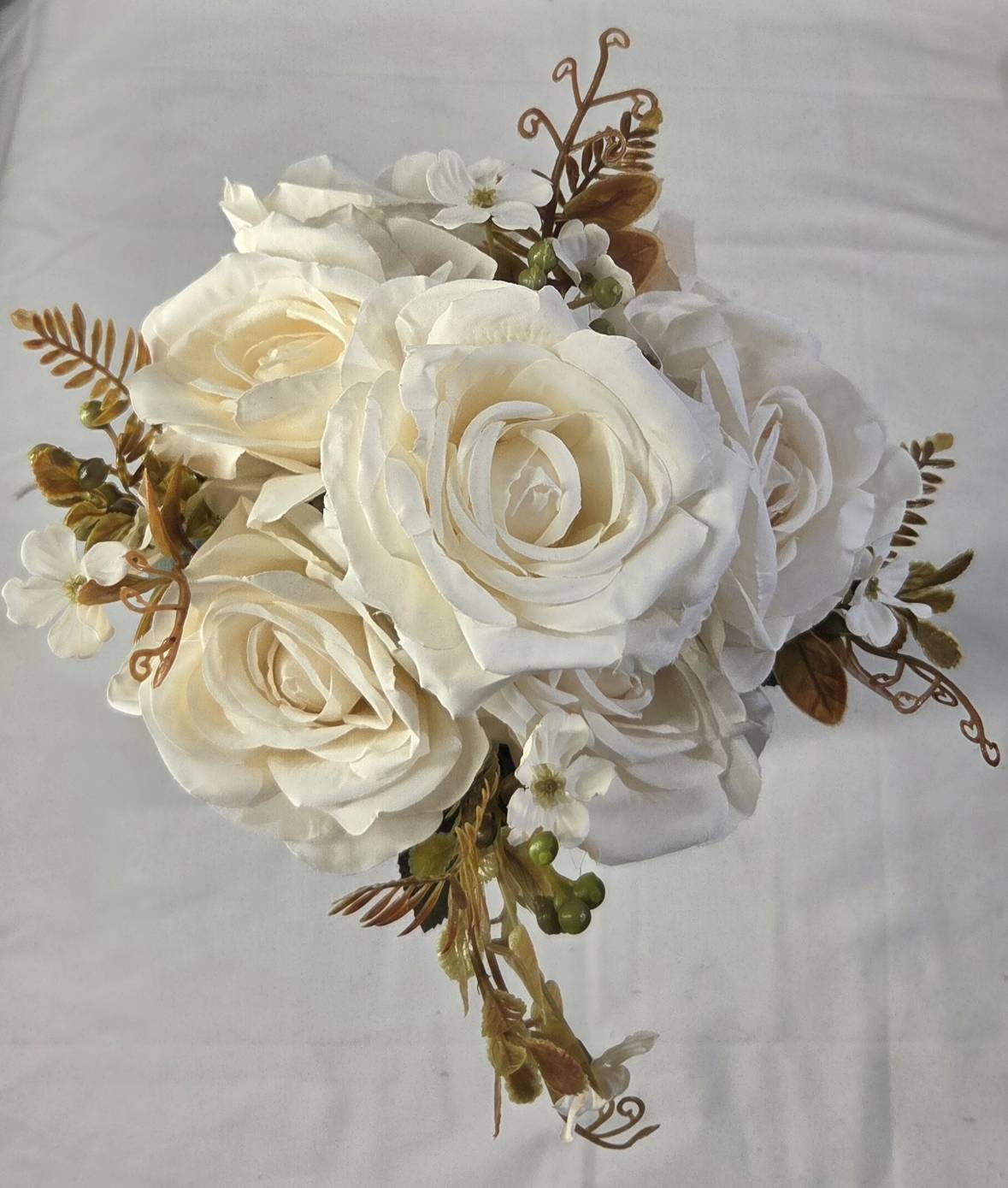 Top view of faux ivory white rose bouquet with aged bronze fern leaves, curling tendrils and white wildflower accents