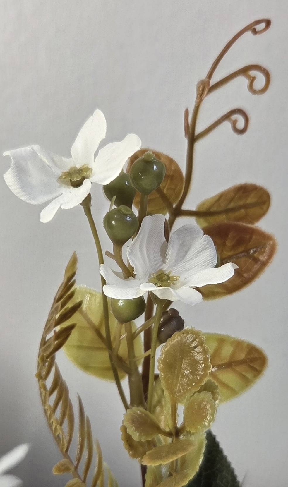 Close-up of faux accent stem with white wildflowers, glossy olive green berry clusters and aged bronze curling tendrils