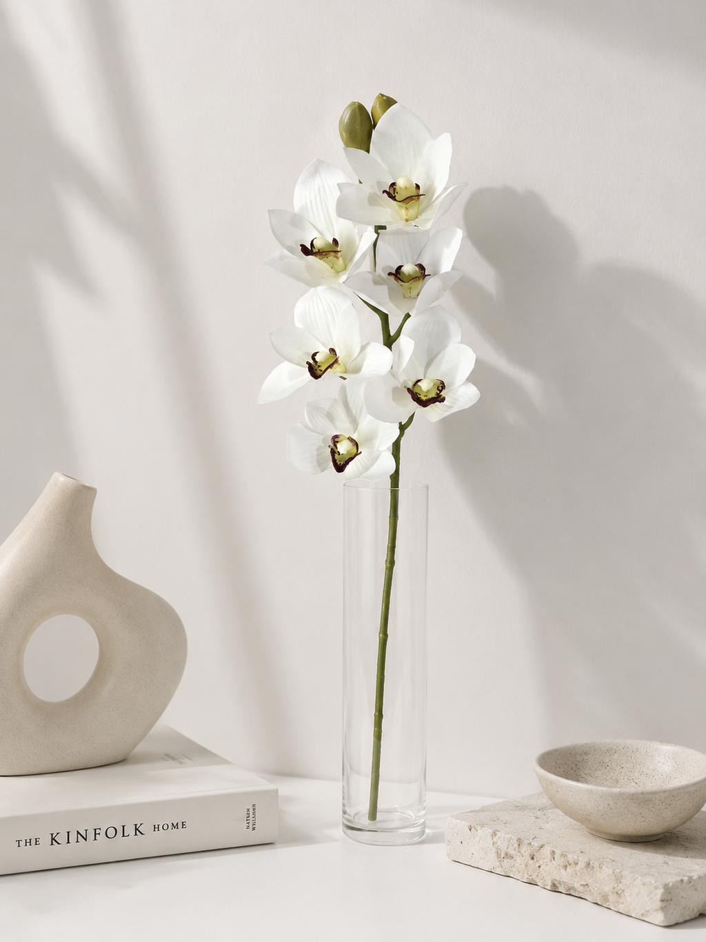 Faux White Cymbidium Orchid Stem ORA-01 - styled in tall glass vase on white table with ceramic decor