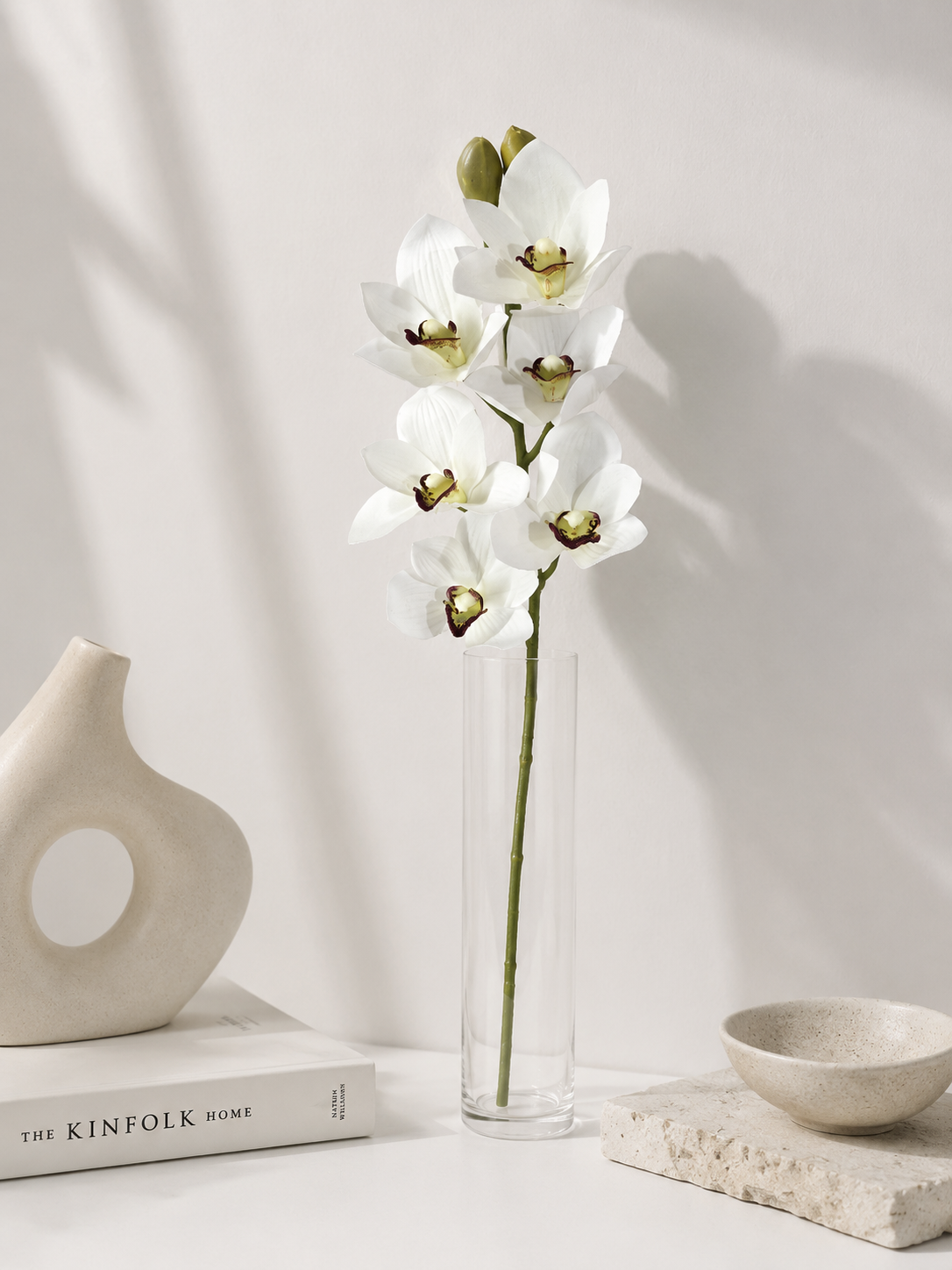 Faux White Cymbidium Orchid Stem ORA-01 - styled in tall glass vase on white table with ceramic decor