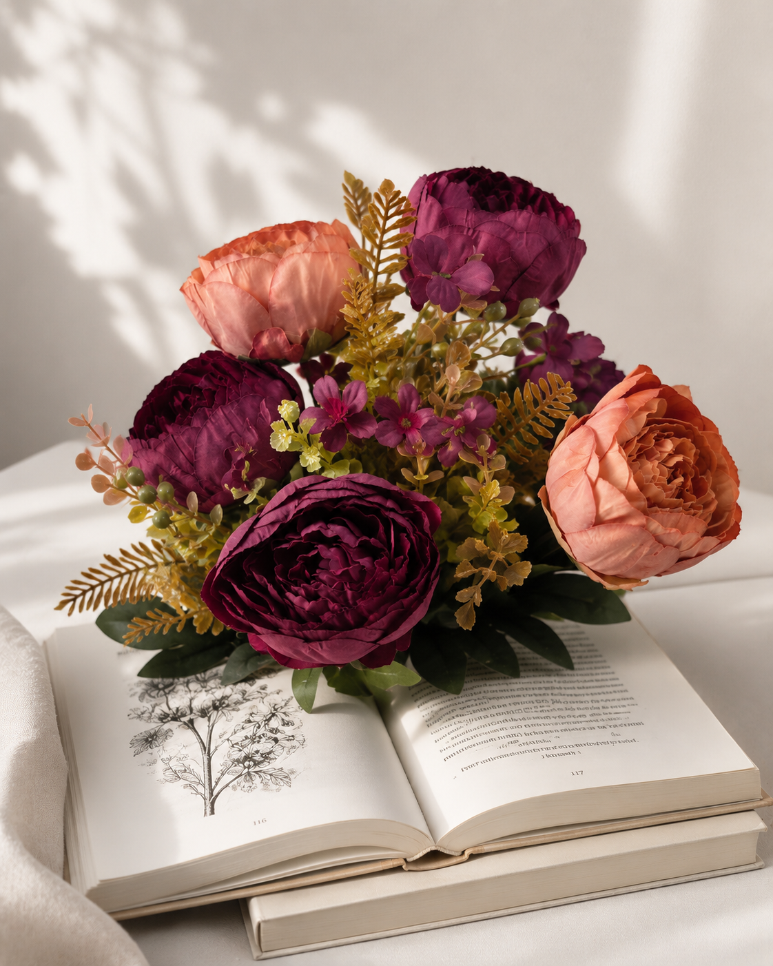 Faux Peony Rose Bouquet ROS-06 lifestyle - burgundy and terracotta peony bouquet arranged on open book with golden fern accents